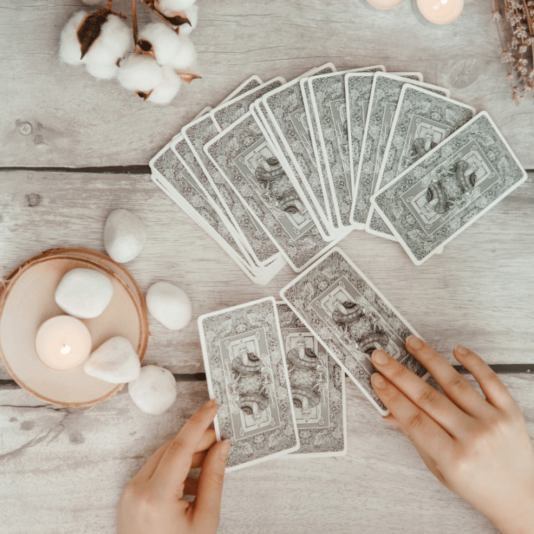 pair of hands reviewing white tarot cards on a wooden table covered in crystals and candles