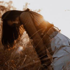 A woman leans down into a field of wheat at sunset.