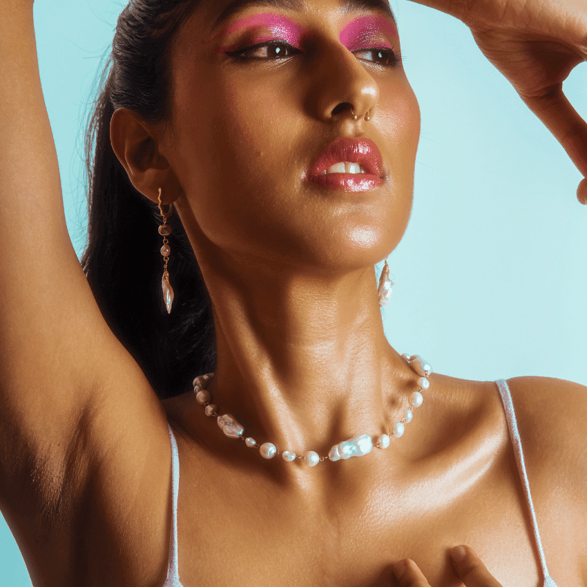 A woman wearing bright pink eyeshadow holds her hand above her head.