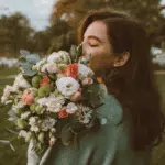 A woman with her eyes closed holds a large bouquet of flowers and appears to smell them.