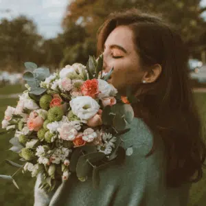 A woman with her eyes closed holds a large bouquet of flowers and appears to smell them.