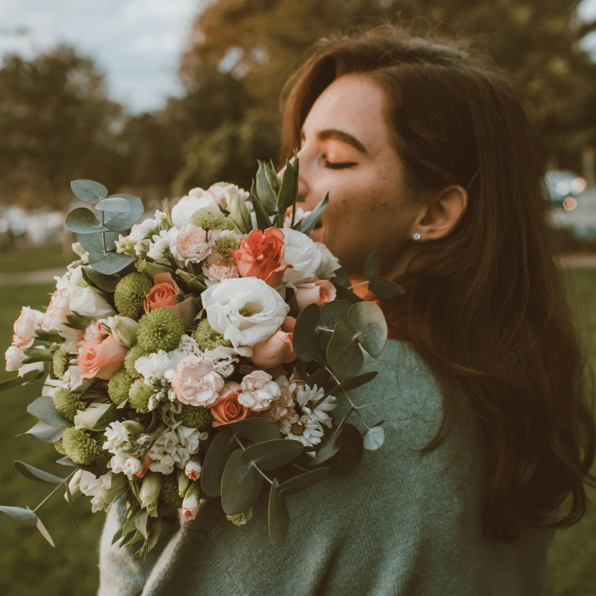 A woman with her eyes closed holds a large bouquet of flowers and appears to smell them.