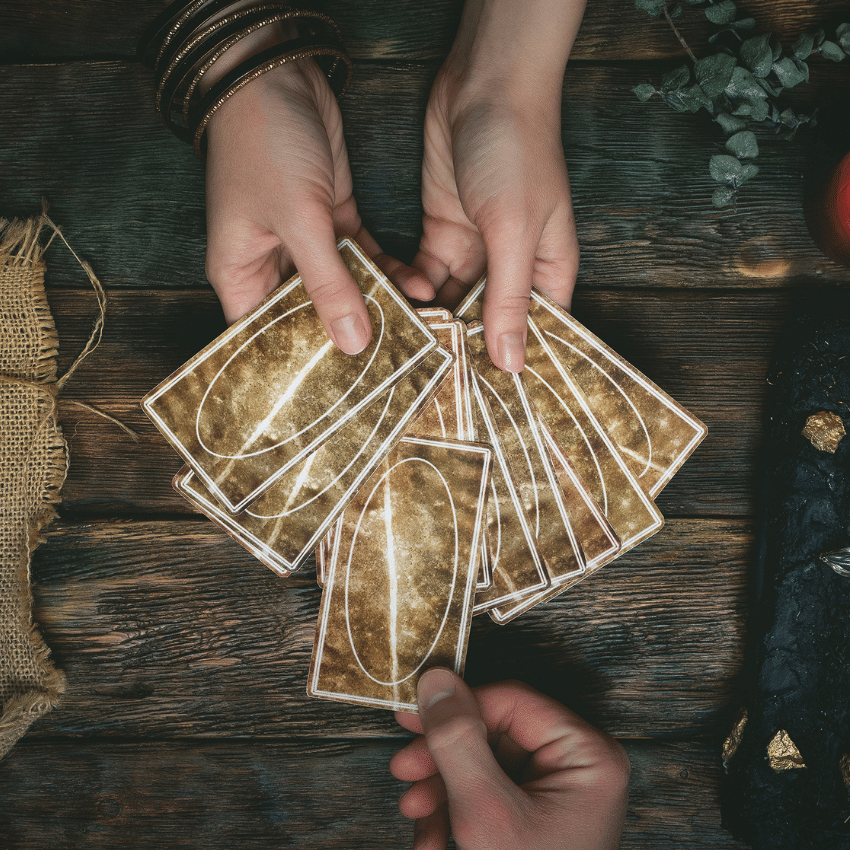 Someone's hands hold a handful of fanned out Tarot cards facing down. Someone else is choosing a card out of the fan.