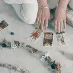 someone crouching on the ground and holding their hands over tarot cards with a line of different color crystals