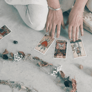 someone crouching on the ground and holding their hands over tarot cards with a line of different color crystals