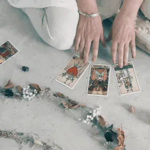 someone crouching on the ground and holding their hands over tarot cards with a line of different color crystals