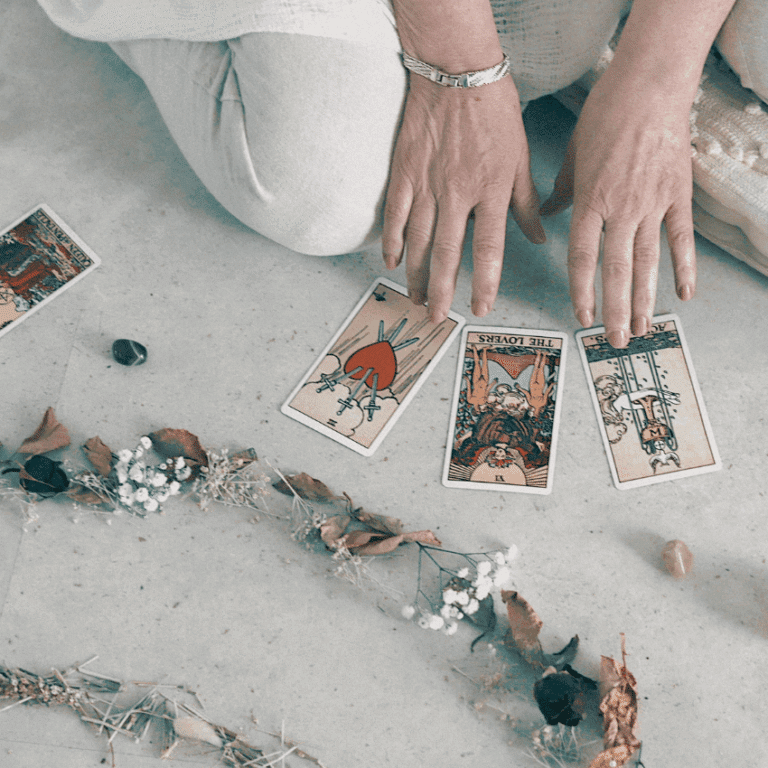someone crouching on the ground and holding their hands over tarot cards with a line of different color crystals