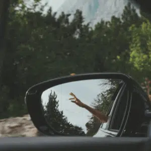 A hand point towards the sky in a rear view mirror of the car. past the mirror is a forest and mountain to represent the final week of Taurus season energy for this week's astrological forecast.