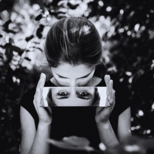 A black and white image of a woman looking down into a rectangular mirror, reflecting her eyes.