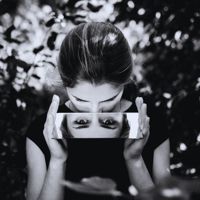 A black and white image of a woman looking down into a rectangular mirror, reflecting her eyes.