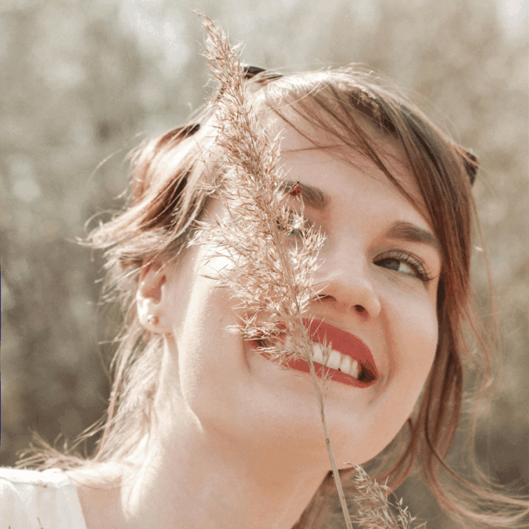 A woman with brown hair smiles at a ladybug on a piece of wheat.