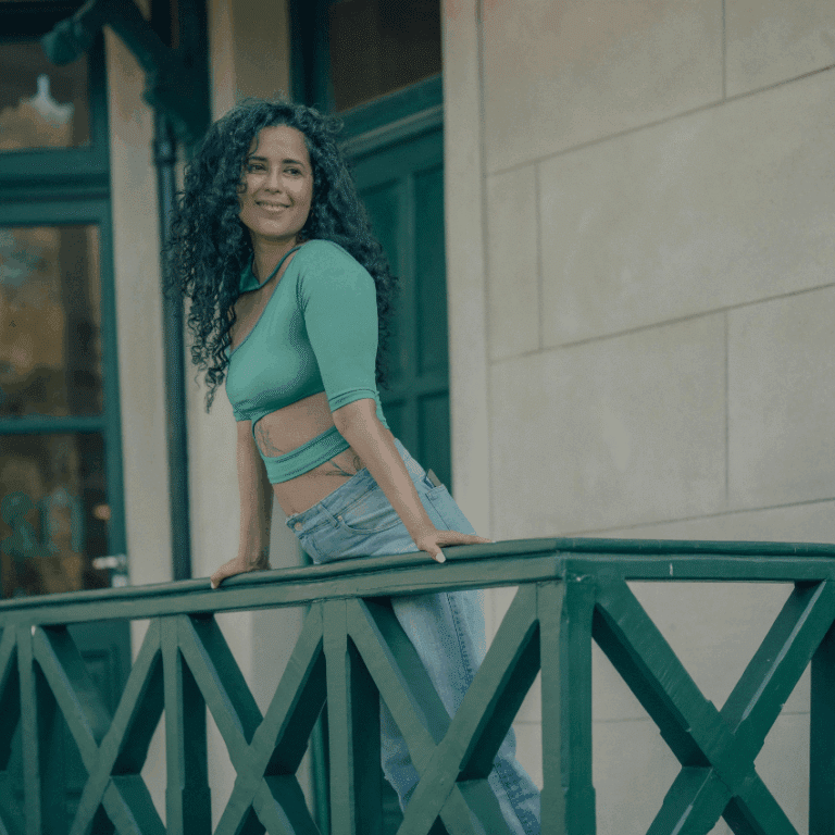 A woman wearing emerald green stands on a balcony with a smile on her face.