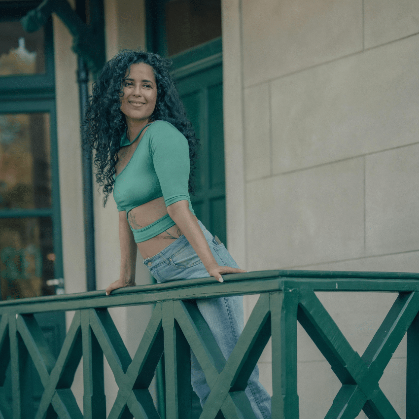 A woman wearing emerald green stands on a balcony with a smile on her face.