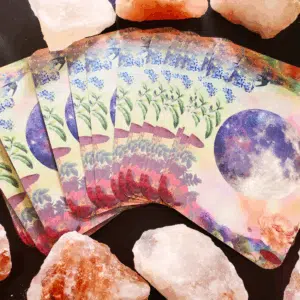 A colorful Tarot deck is spread out on a black table with pink crystals surrounding them.