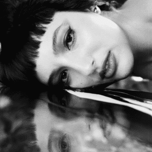 A black and white image of a woman laying on a mirror, her reflection showing up under her.