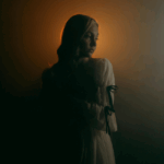A woman faces her left side in shadow but behind her head is illuminated in a soft orange light, representing the crescent of the first quarter moon phase.