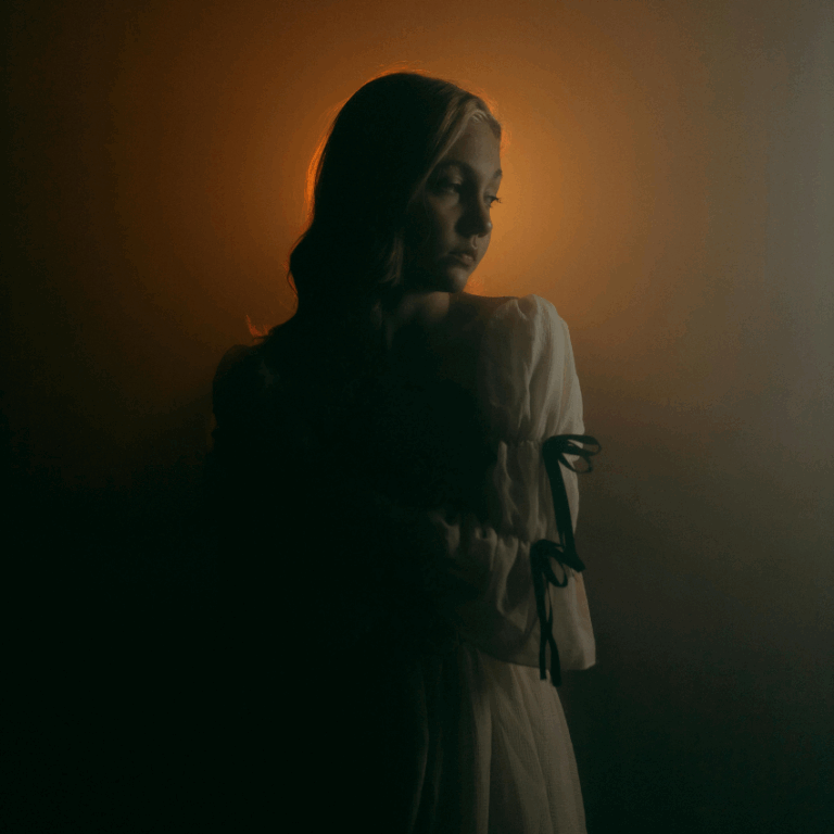 A woman faces her left side in shadow but behind her head is illuminated in a soft orange light, representing the crescent of the first quarter moon phase.