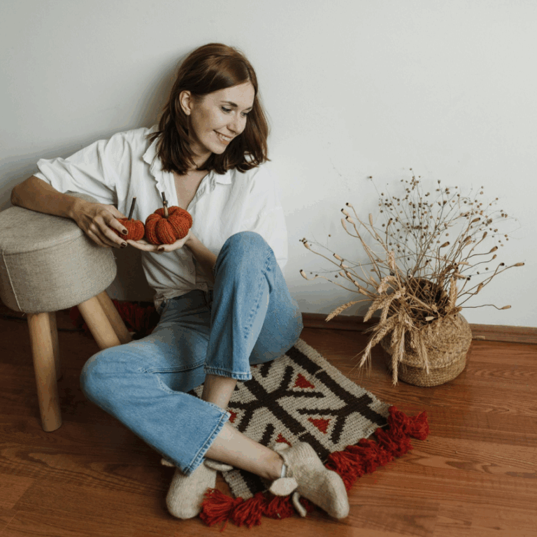 A woman holds a fabric pumpkin, surrounded by modern decorative items, representing the abundance of October.