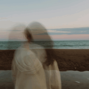 A blurred image of a woman standing next to a body of water to represent the Pisces Lunar Eclipse.