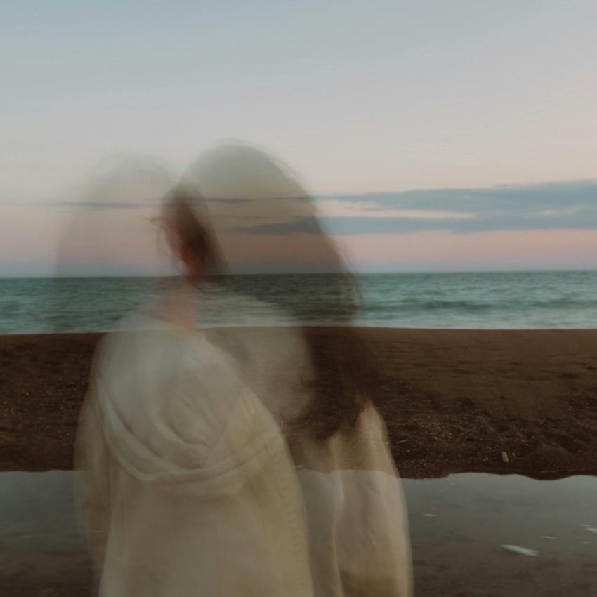 A blurred image of a woman standing next to a body of water to represent the Pisces Lunar Eclipse.