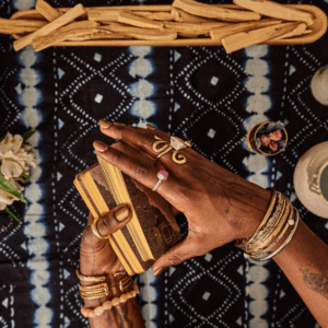 A pair of hands wearing many rings holds a set of Tarot cards, poised to shuffle them.