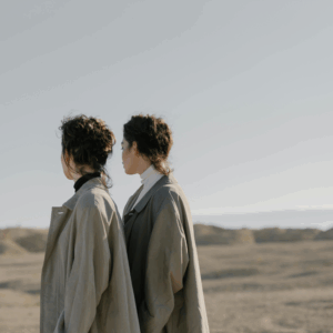 Twins stand in a vast landscape with their backs turned to the camera.