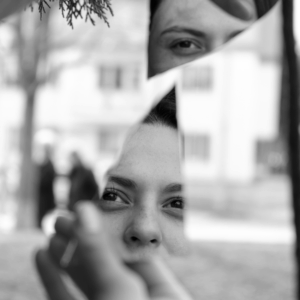 A black and white image of a person looking in a shard of a mirror, symbolizing the weekly astrology reflection to do this week.