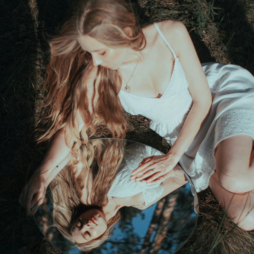 A woman with long hair looks into a mirror, reflecting back at her.