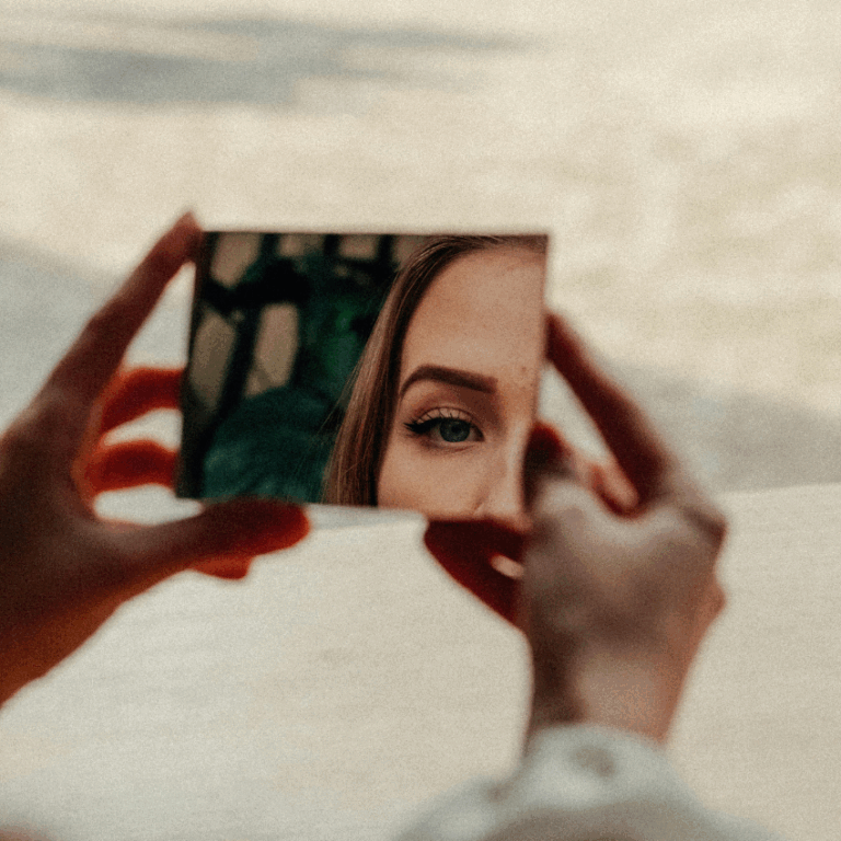 Two hands hold a rectangular mirror with a woman's face reflected back representing the reflection to do with astrology this week.