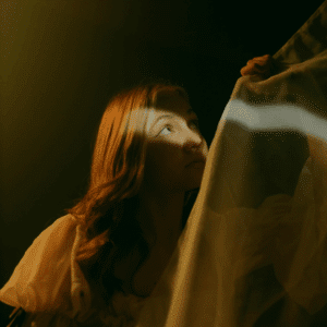 A woman peers up, a sliver of light hitting her face to represent the light of the last quarter Moon phase.