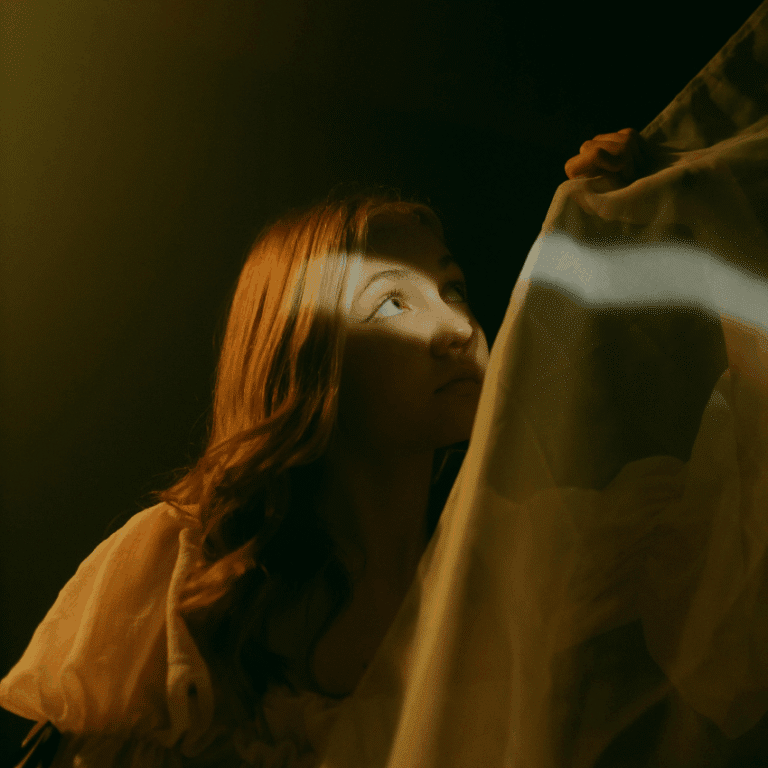 A woman peers up, a sliver of light hitting her face to represent the light of the last quarter Moon phase.