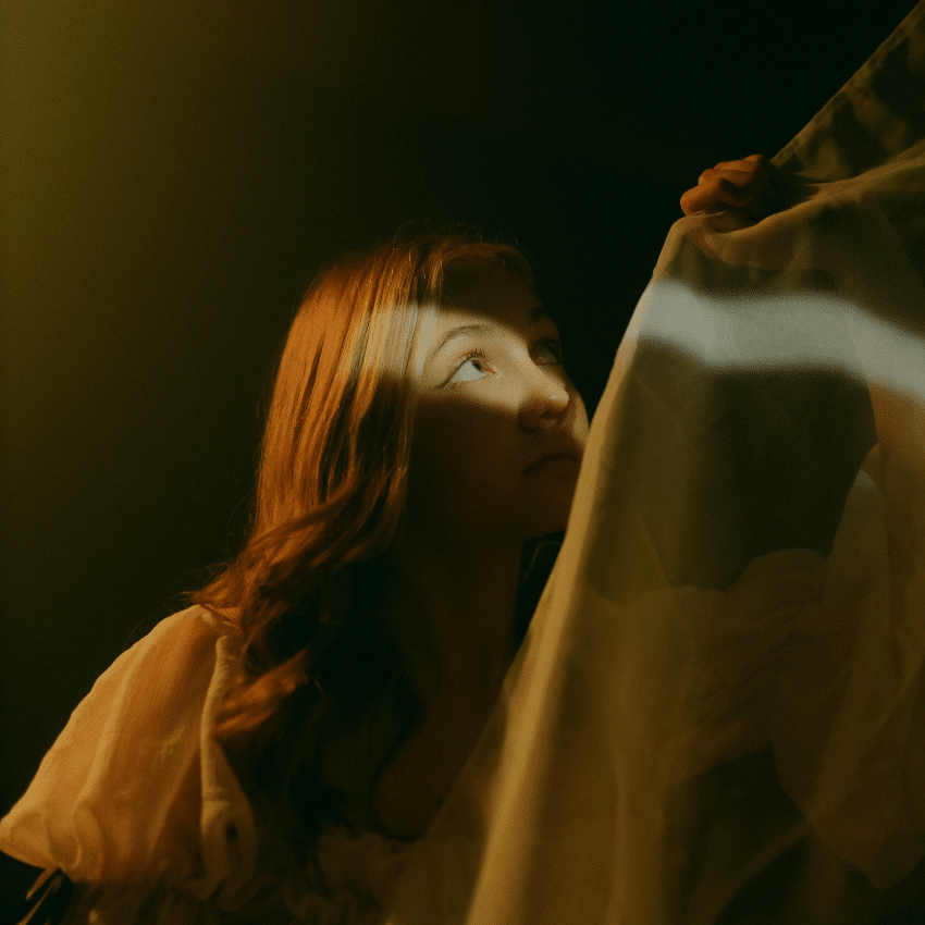 A woman peers up, a sliver of light hitting her face to represent the light of the last quarter Moon phase.