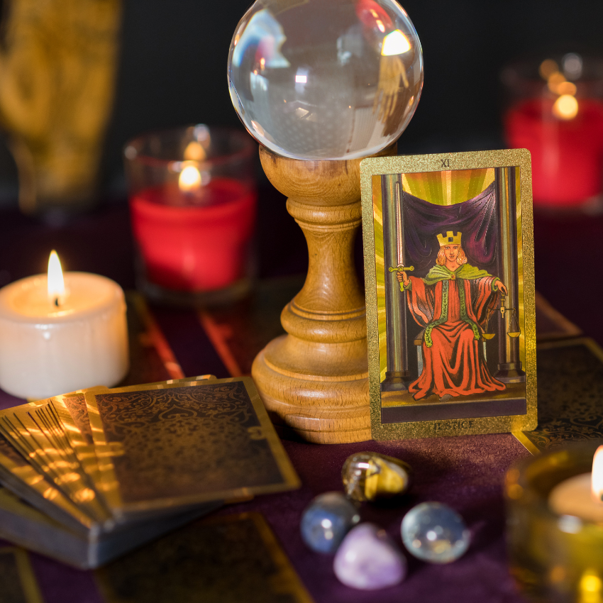 A Tarot card of Justice upright amongst red and white candles, representing the bold energy of December 2025 Tarotscopes.