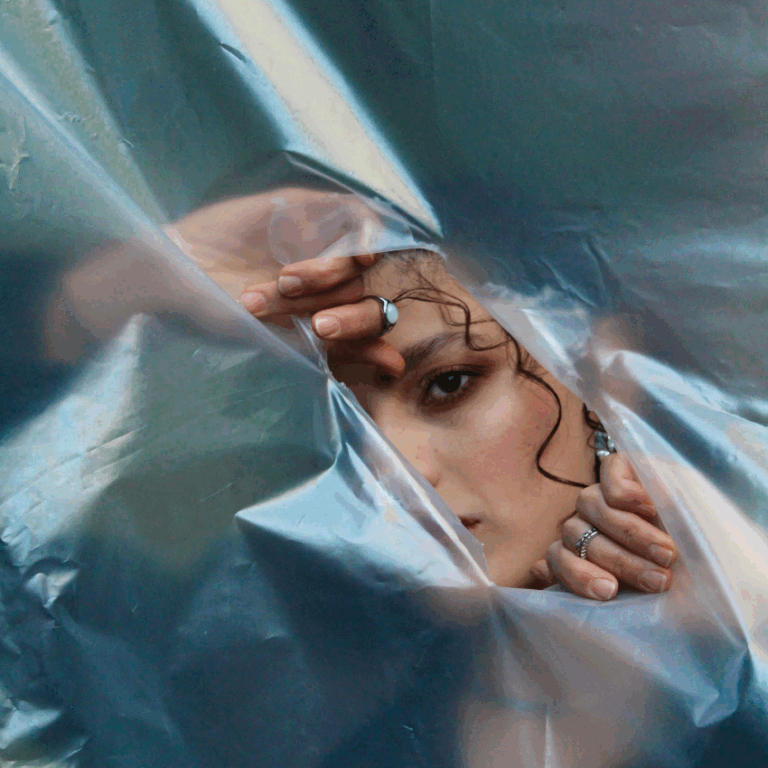 A woman appears to be breaking through a piece of paper, her eye and cheek showing.