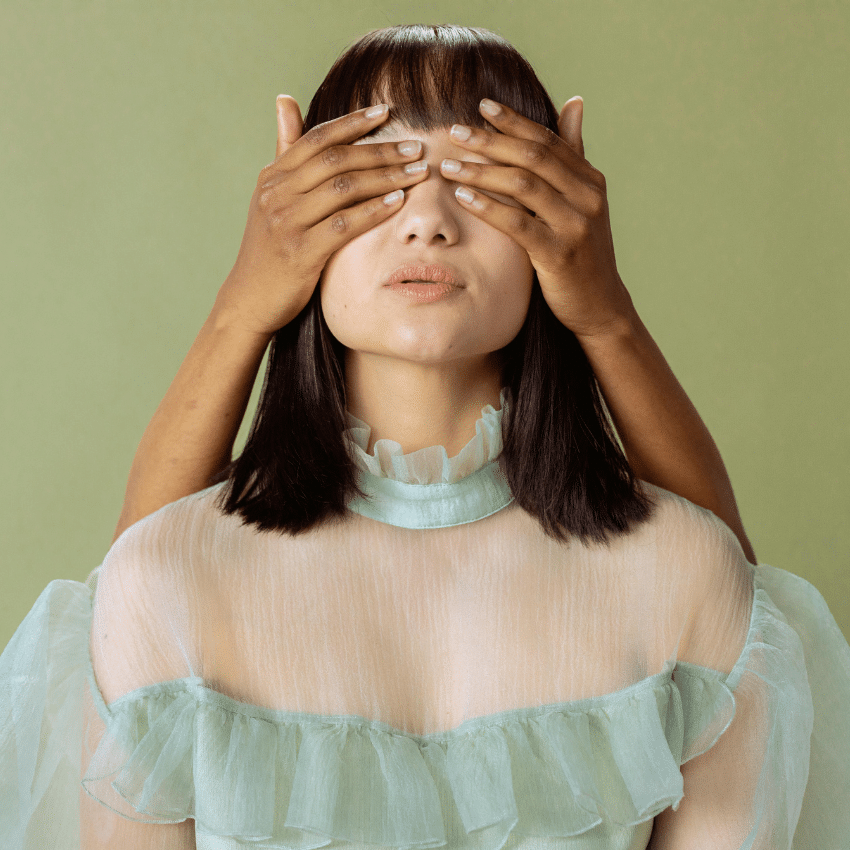 A woman wearing a green dress has someone else's hands covering her hands, representing the backwards energy of Mercury retrograde.