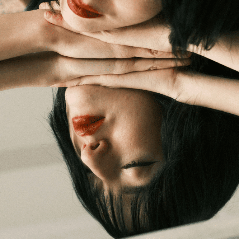 A woman rests her head on a mirror, her reflection showing to represent weekly astrology energy.