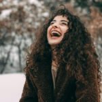 A woman with curly hair laughs. The weather around her looks snowy and crisp to represent the winter of Capricorn season.