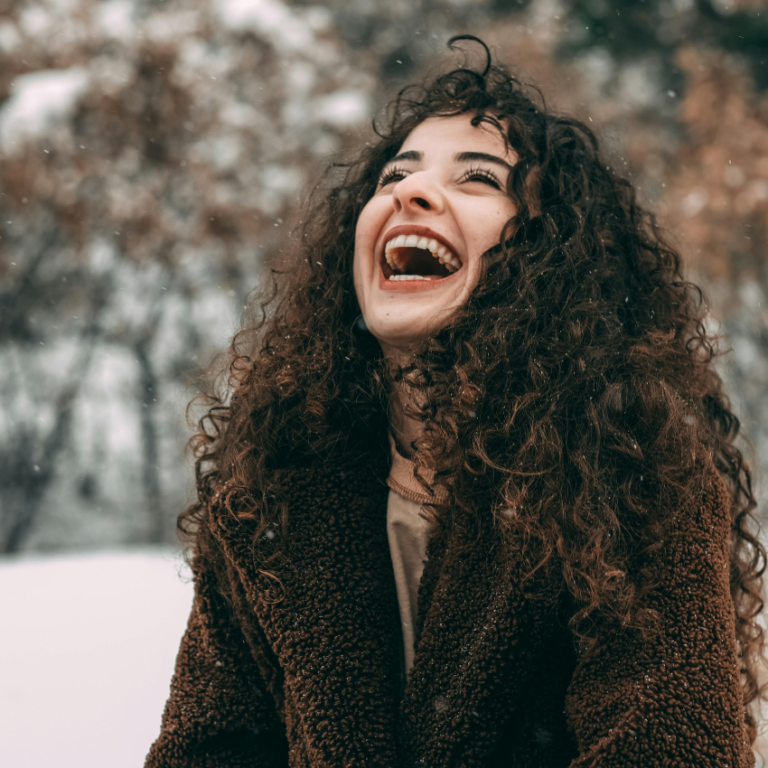 A woman with curly hair laughs. The weather around her looks snowy and crisp to represent the winter of Capricorn season.