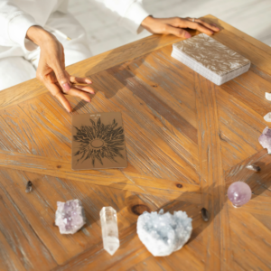 A woman's hands are shown hovering over a Tarot deck and the back of a Tarot card. There are crystals on the table in front of her.