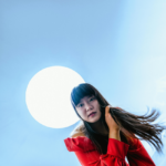 A woman with long black hair wearing a red top stands slightly in front of a large moon-like orb, representing the 2026 moon events.