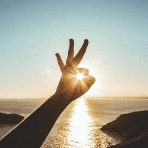 Someone holds their hand up to the sun on the horizon, forming an "ok" sign around it.