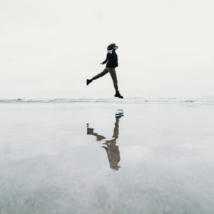 A woman jumps over a puddle, reflecting her image back to represent the water bearer energy of Aquarius season during February 2026.