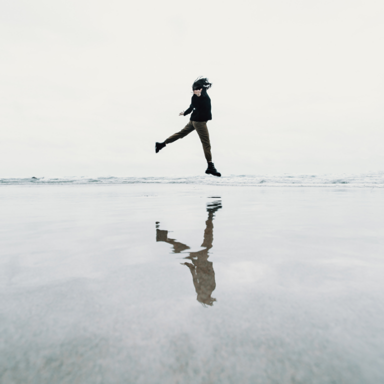 A woman jumps over a puddle, reflecting her image back to represent the water bearer energy of Aquarius season during February 2026.