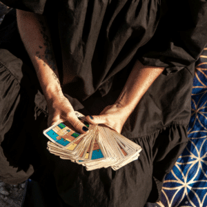 A woman wears a black dress and holds Tarot cards fanned out in front of her.