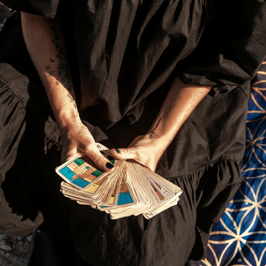 A woman wears a black dress and holds Tarot cards fanned out in front of her.