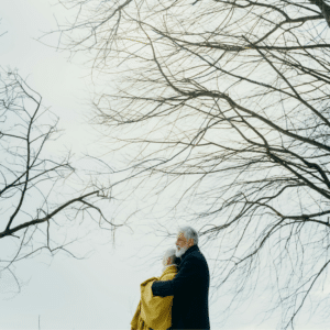 An older couple stands together looking up at the sky and trees.