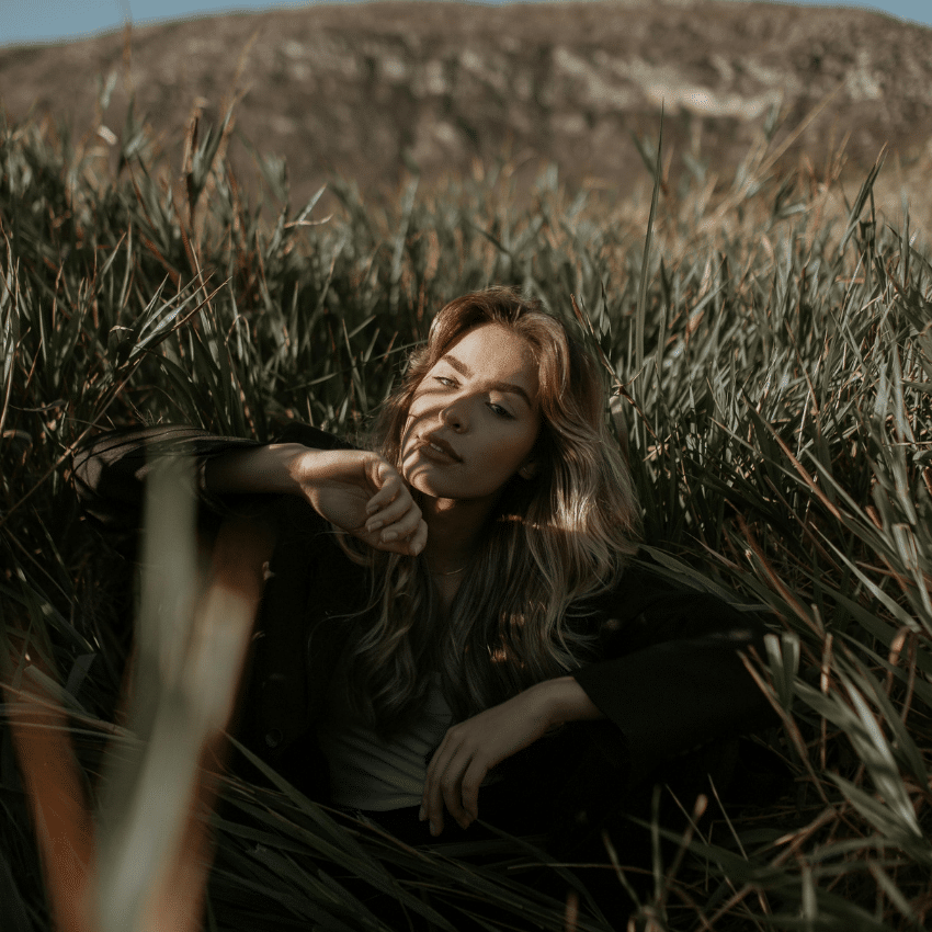 A woman sits in tall grass, representing the earthy nature of Taurus.