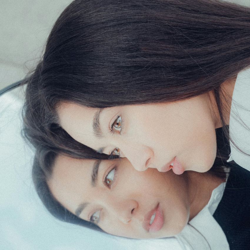 A woman has her head against a mirror, her reflection representing this week's astrology energy and the reflections we should take to make the most of the energy.