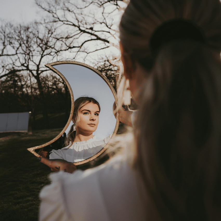 A woman looks into a crescent moon-shaped mirror, to represent the quarter moon phase occurring in this week's astrology.