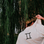 A man holding up the back of his shirt which has the Gemini symbol on it to represent the Moon in Gemini energy.